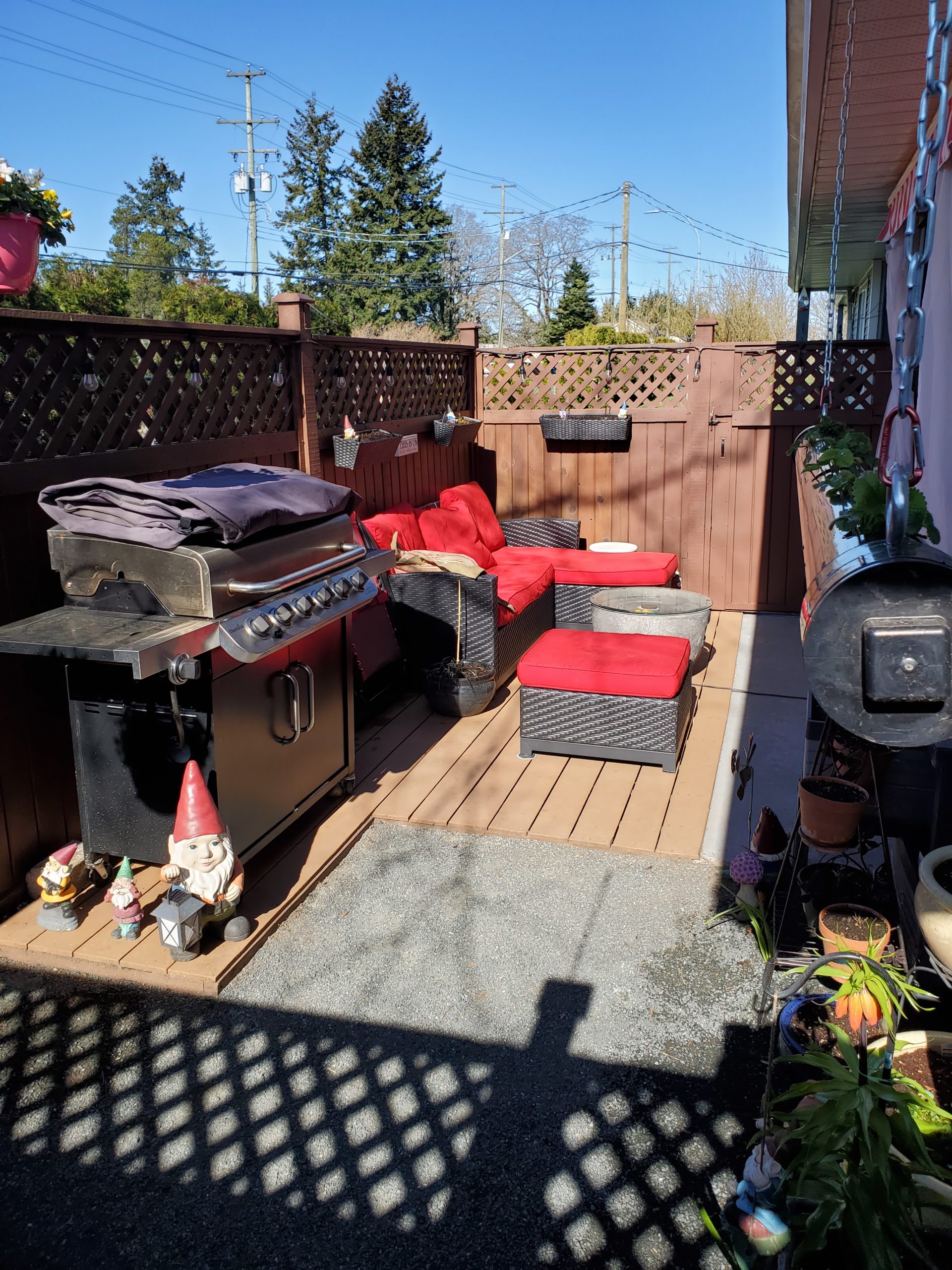 A patio lounge with red furniture sits in the sunlight with garden gnomes in front.