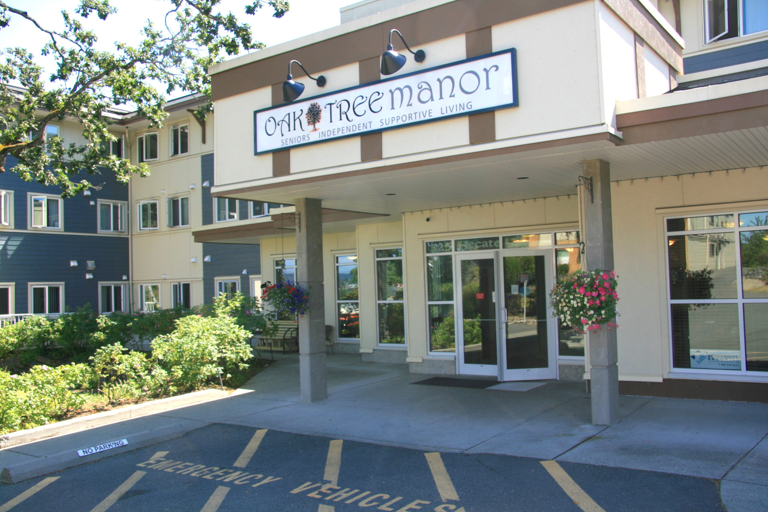 The front entrance of Oak Tree Manor's affordable seniors’ home shows a three-storey complex with a hanging basket at the front window.