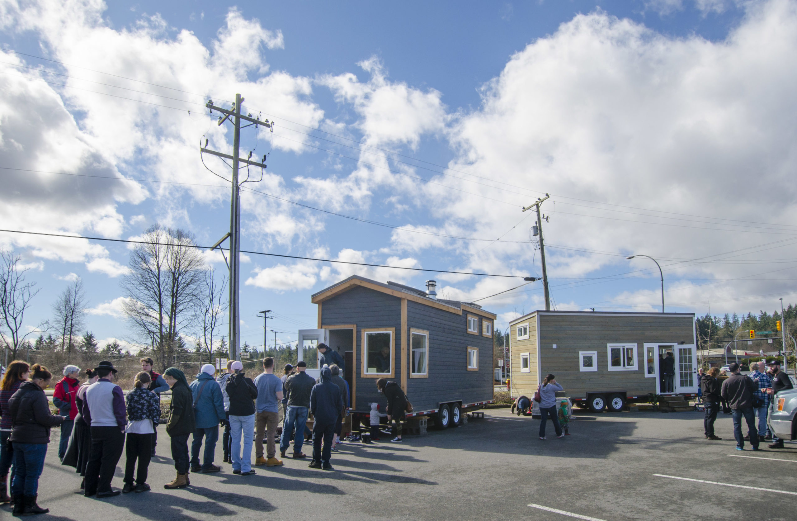 A large crowd likes up to view Rewild Tiny Homes in a parking lot in Nanaimo with clear blue skies pre-pandemic.
