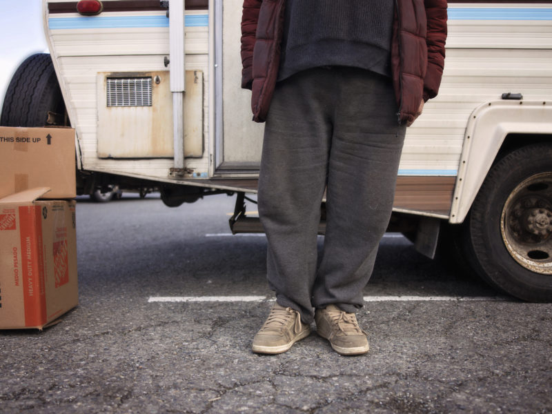 John, a low-income senior in Nanaimo, is shown standing in front of his RV from the chest down.