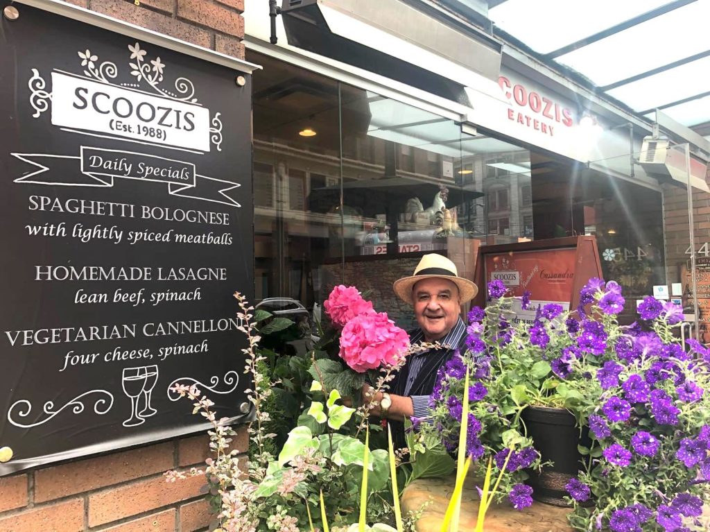 Former owner of Nanaimo's Chez Michel Michael Stamoulis stands in the entrance of Vancouver's Scoozis Restaurant amidst flowers.