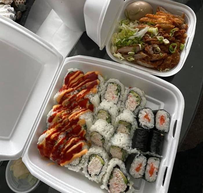 Two takeout containers filled with sushi rolls sit side by side.