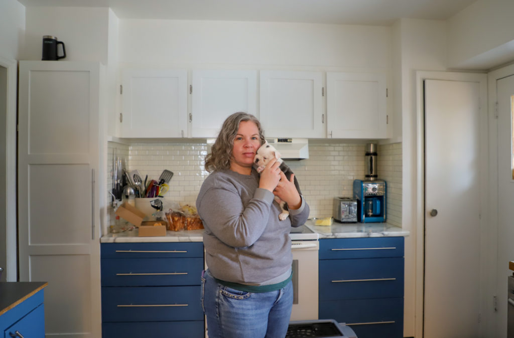 A Nanaimo renter holds a puppy in her blue and white kitchen at the home she currently rents for her family.