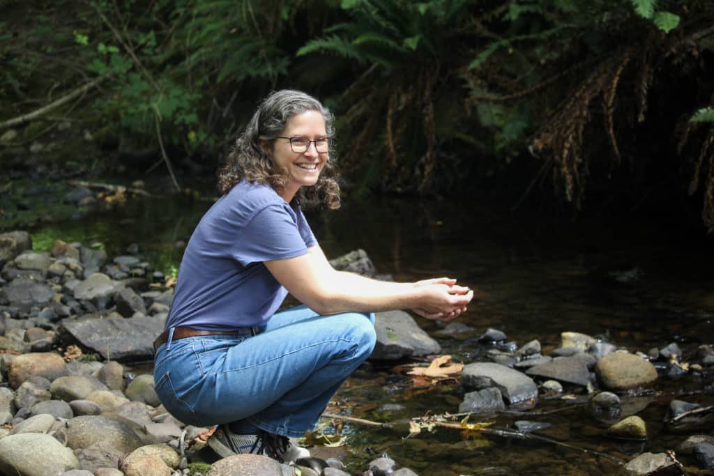 Jennifer Shepherd crouches along the bed of a creek, looking at the camera and smiling.