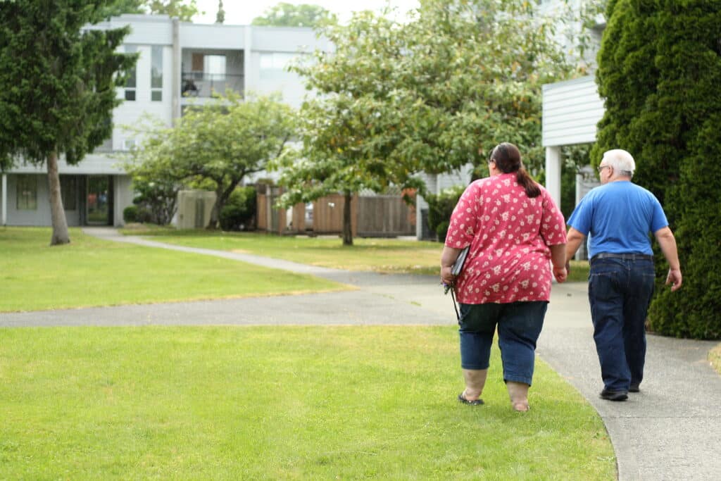 Two people hold hands as they walk on the grounds outside their rental complex.
