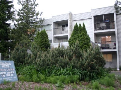 An older rental building with four storeys and balconies is nestled in trees. A sign reads Willow Estates.