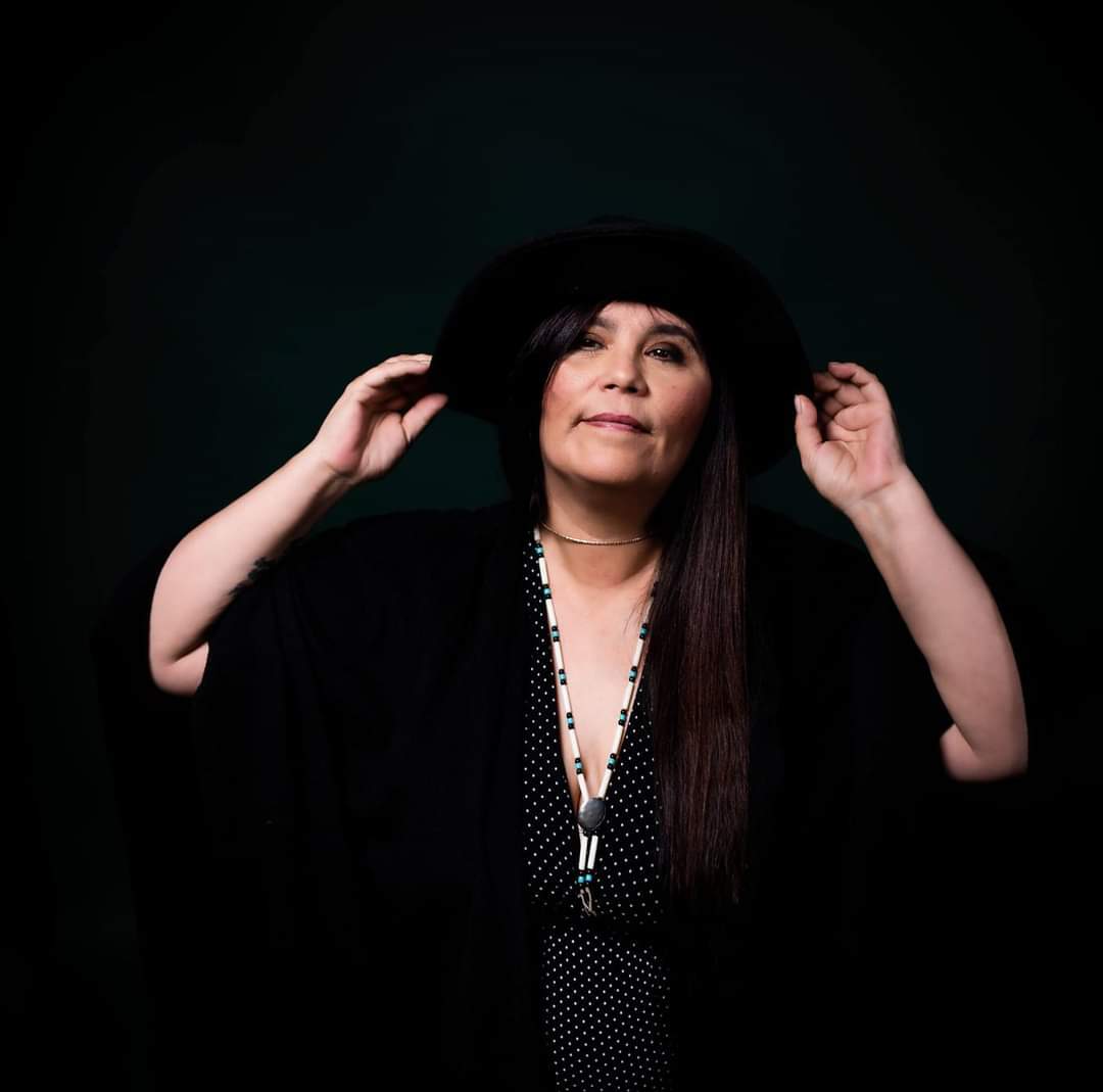 A woman in black raises her hands against a black background.