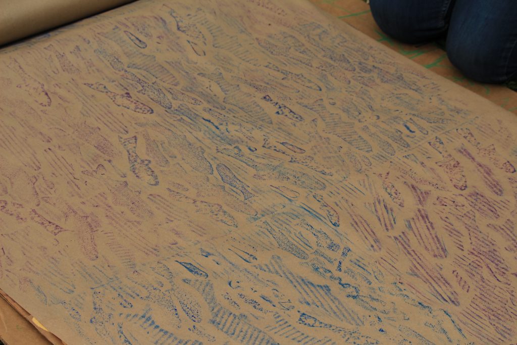 A brown piece of paper with images of fish that have been coloured on using stencils underneath.