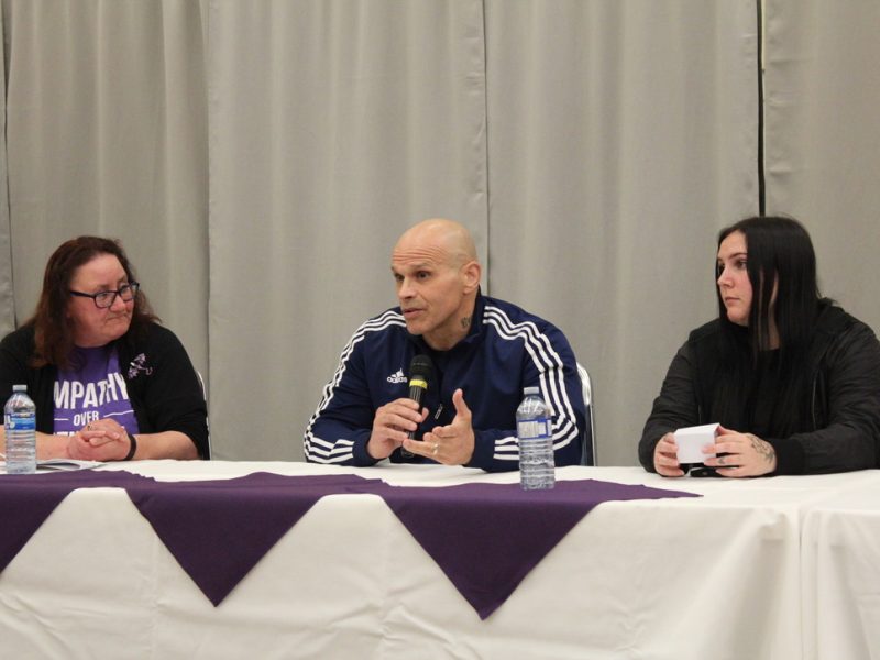 Three people sit at a table as part of a panel discussing the toxic drug crisis in Cowichan. A man in the centre and a woman on either side.